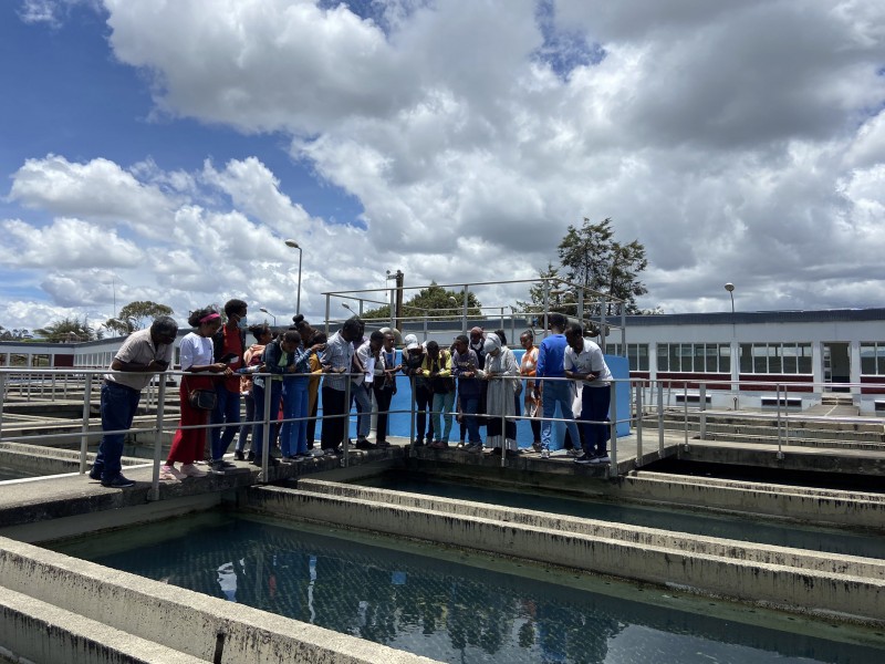 Researchers and school pupils look over metal railings at water treatment tanks below during a tour of the Legedadi water treatment plant